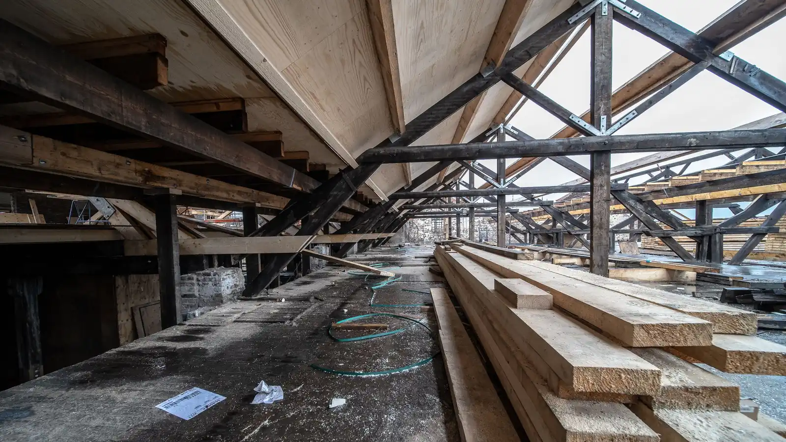 Combles en rénovation : charpente ancienne et bois neuf empilé sur le plancher
